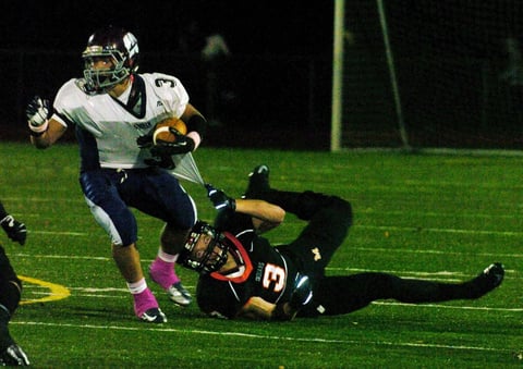 Football player in white uniform evading tackle from defender in black uniform during night game on lit field